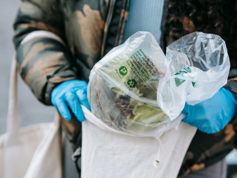 Gloved hand holding a shopping bag filled with fresh leafy produce