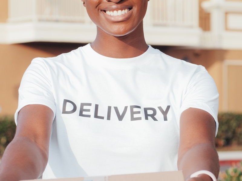 Smiling delivery worker in a white DELIVERY t-shirt holding out a package